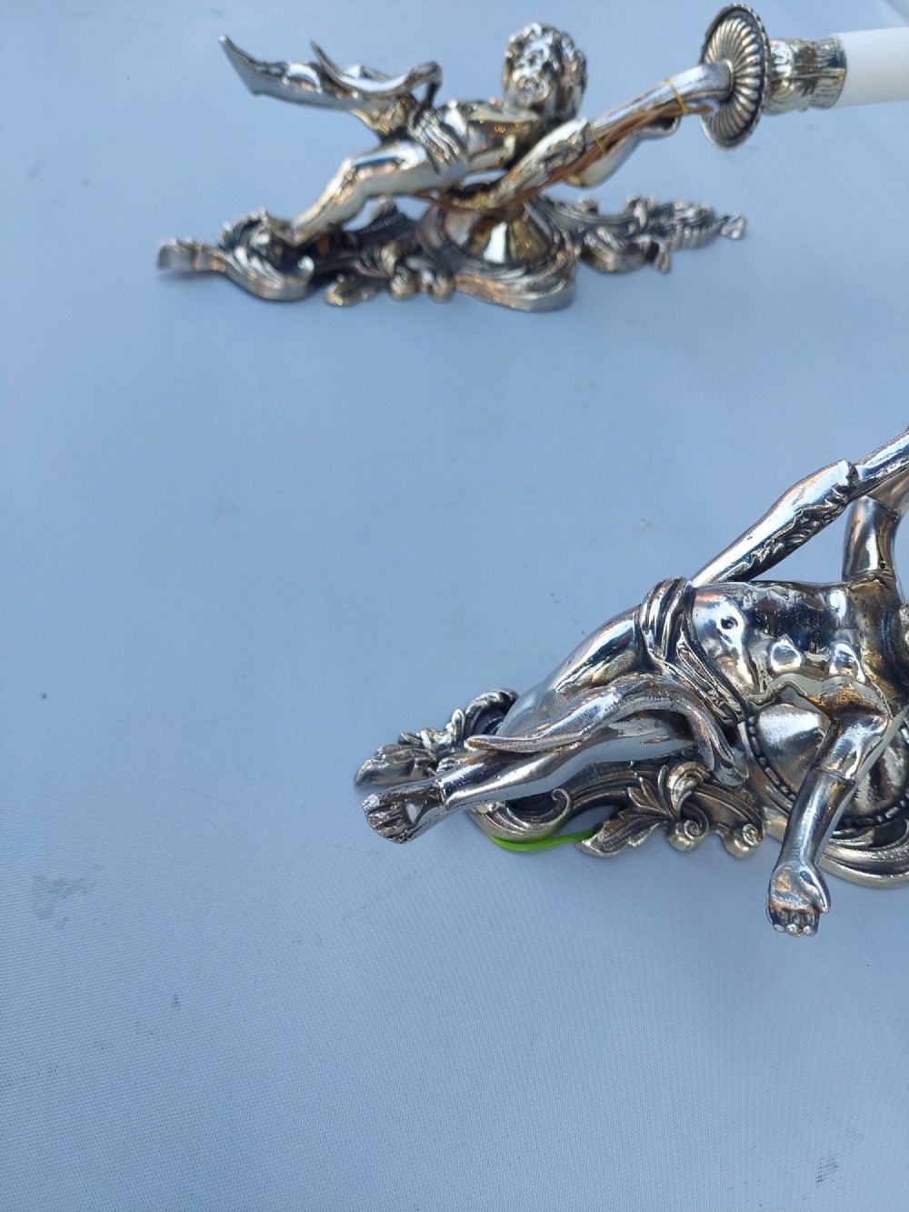 A pair of early 20th-century silvered metal wall sconces featuring sculpted cherubs holding single candle sockets set against elaborate scrollwork backplates. View VII