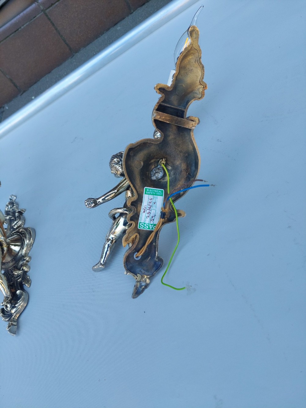 A pair of early 20th-century silvered metal wall sconces featuring sculpted cherubs holding single candle sockets set against elaborate scrollwork backplates. View IX