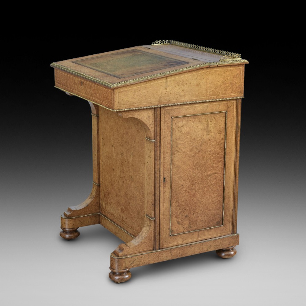 A mid-19th-century Victorian Davenport desk crafted from amboyna veneer with a sloping leather writing surface, decorative brass gallery, and side cupboard door.