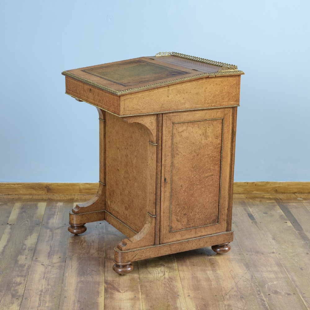 A mid-19th-century Victorian Davenport desk crafted from amboyna veneer with a sloping leather writing surface, decorative brass gallery, and side cupboard door. View V