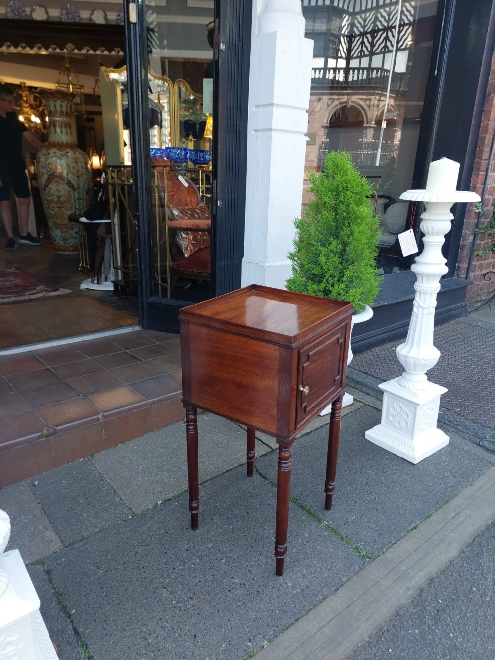 An early 19th-century Regency mahogany bedside cabinet featuring a single panelled door, tray top gallery, turned legs, and a brass knob. View III