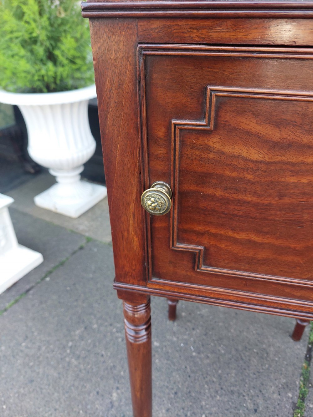 An early 19th-century Regency mahogany bedside cabinet featuring a single panelled door, tray top gallery, turned legs, and a brass knob. View IV