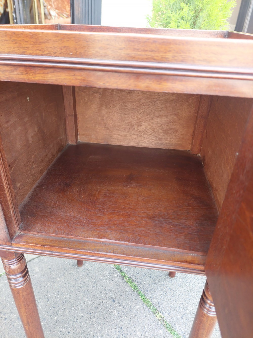 An early 19th-century Regency mahogany bedside cabinet featuring a single panelled door, tray top gallery, turned legs, and a brass knob. View VI