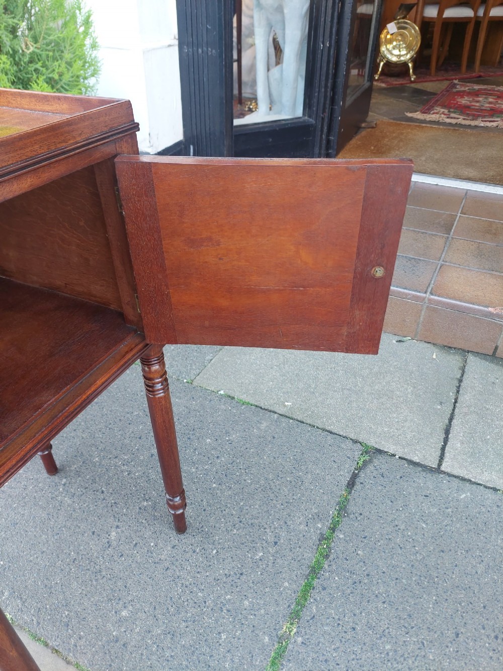 An early 19th-century Regency mahogany bedside cabinet featuring a single panelled door, tray top gallery, turned legs, and a brass knob. View VII