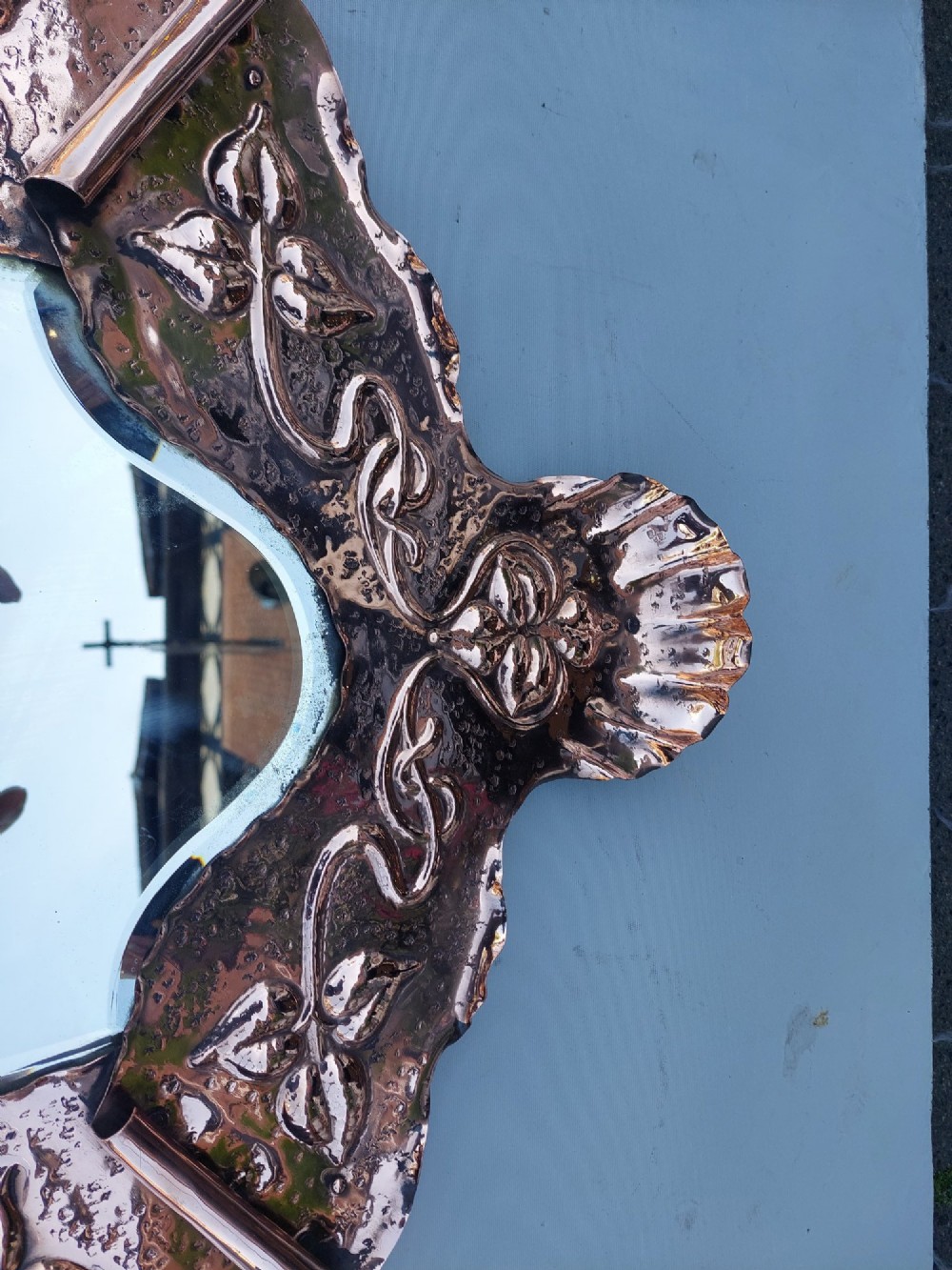 A shield-shaped wall mirror featuring a hand-hammered copper frame decorated with floral repousse motifs and a bevelled glass centre. View II
