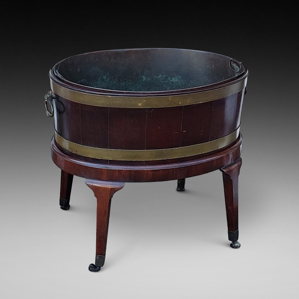 An 18th-century oval dark mahogany wine cooler with brass binding straps and carrying handles, elevated on a four-legged stand with castors.