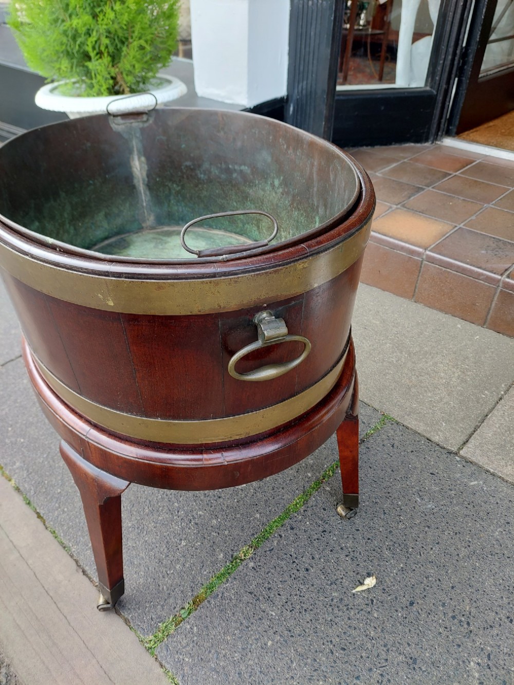 An 18th-century oval dark mahogany wine cooler with brass binding straps and carrying handles, elevated on a four-legged stand with castors. View III