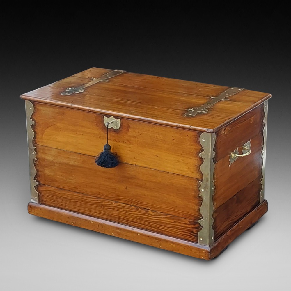 A rectangular Victorian pitch pine storage trunk featuring reinforced brass corner straps, strap hinges, side handles, and a keyhole with a black tassel.