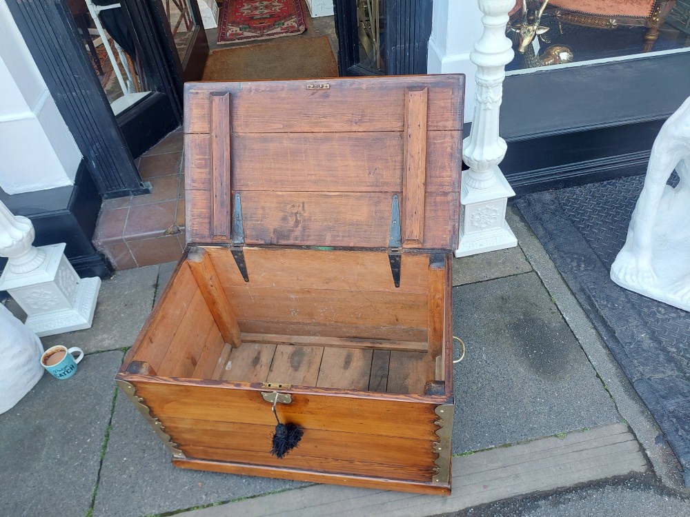 A rectangular Victorian pitch pine storage trunk featuring reinforced brass corner straps, strap hinges, side handles, and a keyhole with a black tassel. View V
