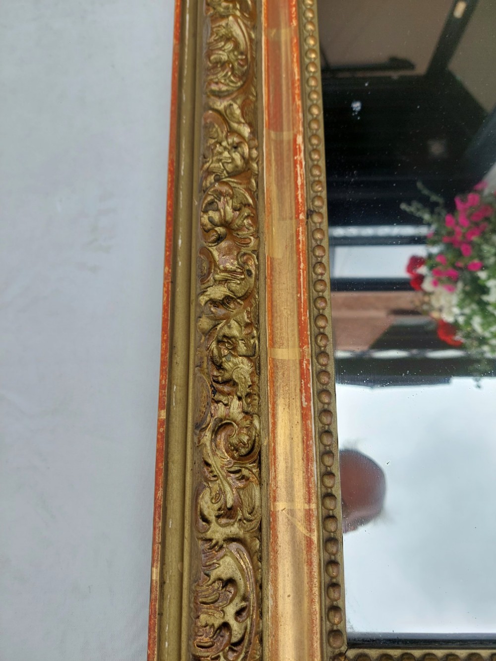 A late nineteenth-century wall mirror featuring an arched giltwood frame with carved foliate details, a beaded inner border, and distressed gold leaf revealing underlying red bole. View III