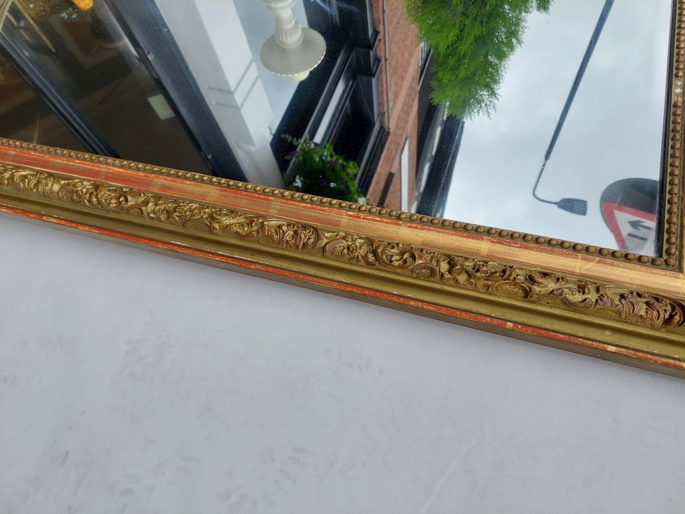 A late nineteenth-century wall mirror featuring an arched giltwood frame with carved foliate details, a beaded inner border, and distressed gold leaf revealing underlying red bole. View IV