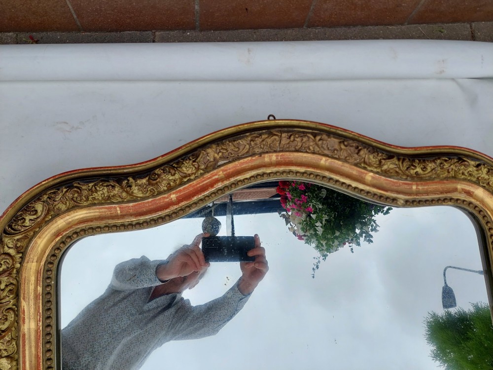 A late nineteenth-century wall mirror featuring an arched giltwood frame with carved foliate details, a beaded inner border, and distressed gold leaf revealing underlying red bole. View VI