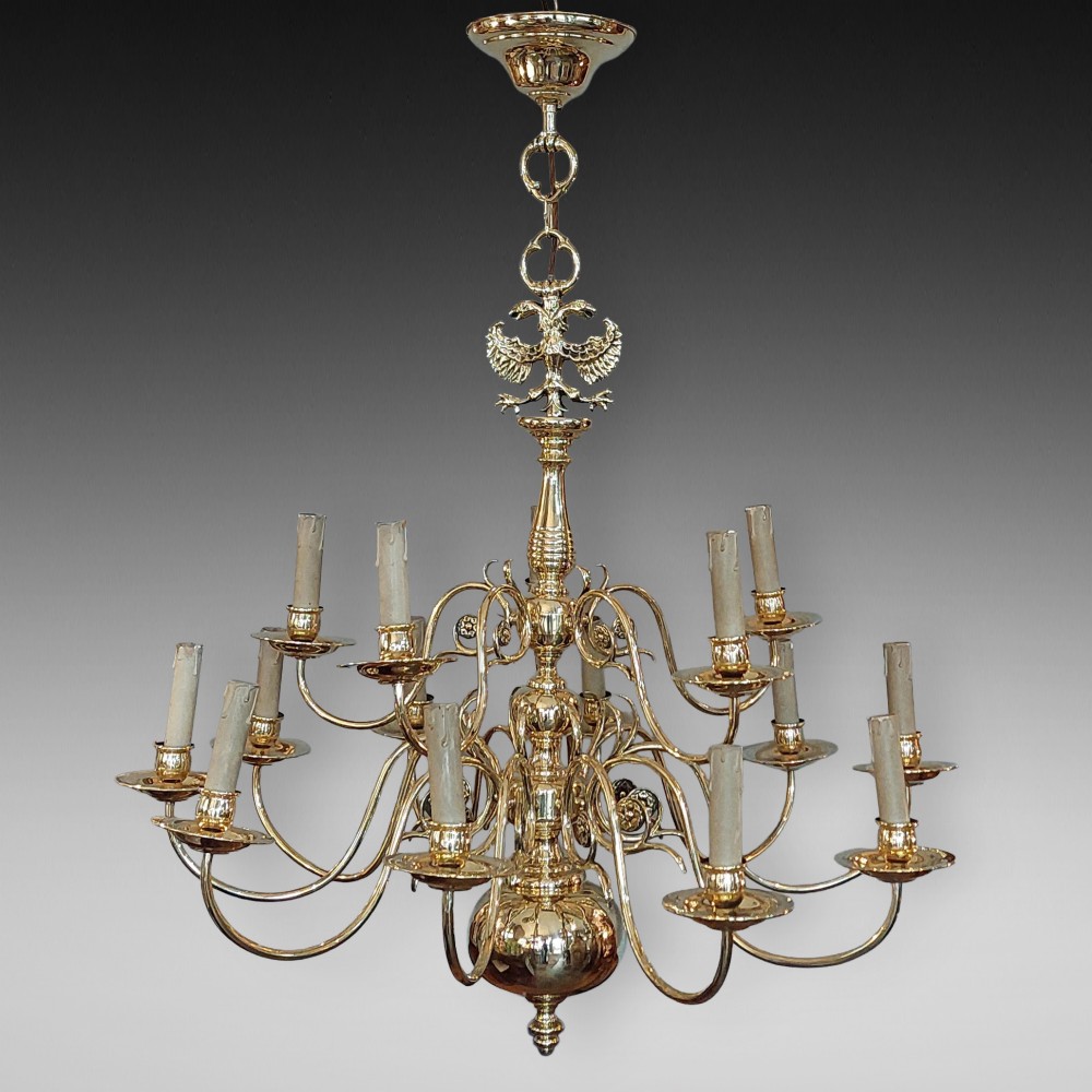 An 18th-century Dutch style polished brass chandelier featuring two tiers of curved arms, candle-style bulb holders, a central baluster stem, and a double-headed eagle crest.