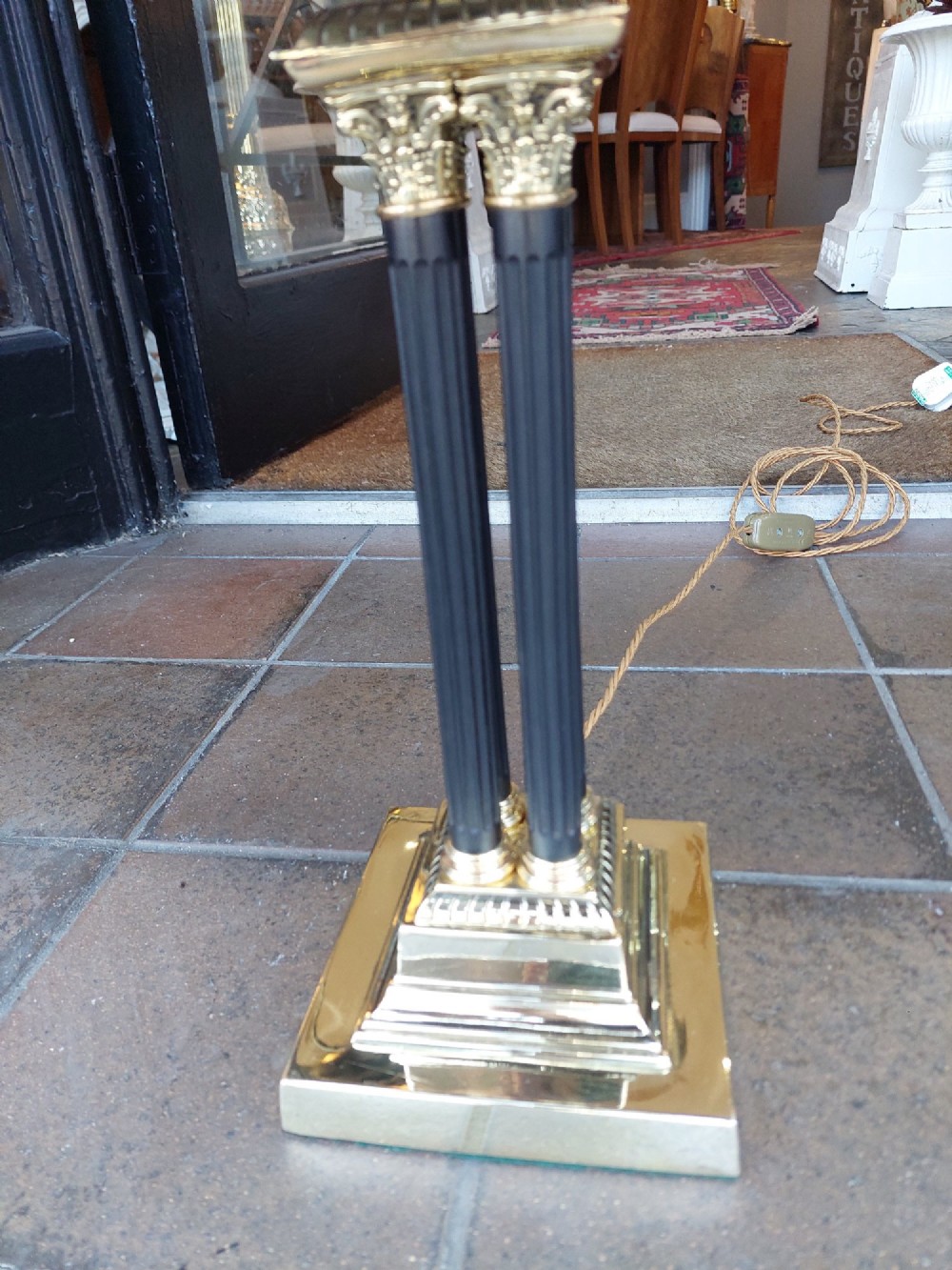 An antique brass table lamp featuring a four-pillar Corinthian column base and a patterned blue dome lampshade with dark fringe. View V