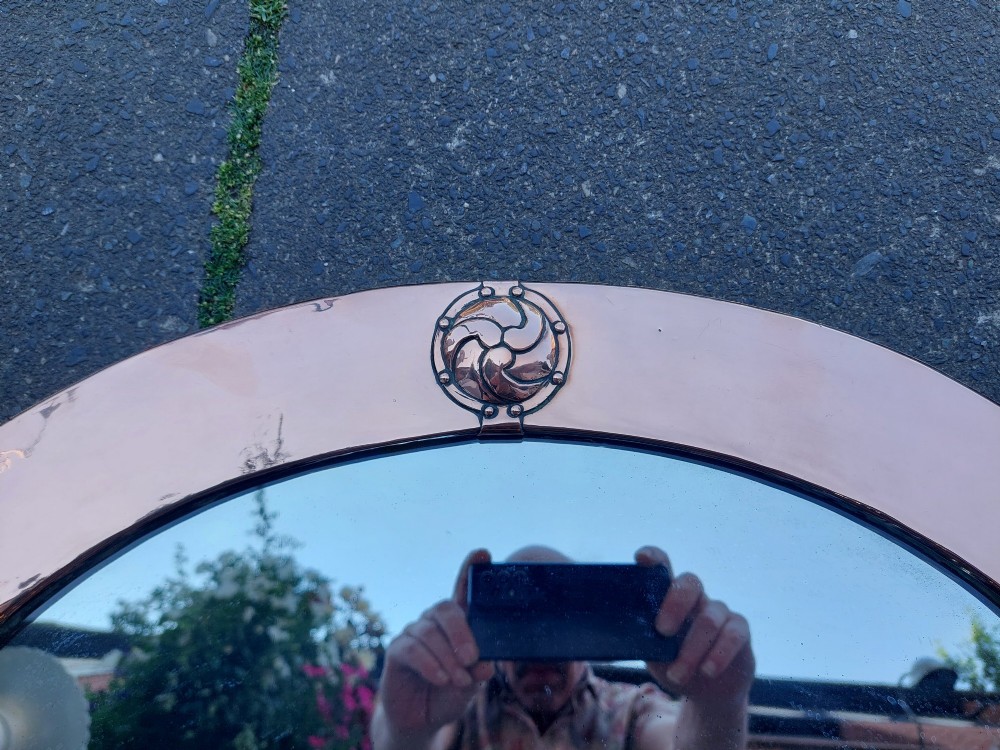 An oval Arts and Crafts wall mirror featuring a polished copper frame embellished with four circular Celtic swirl motif roundels. View II