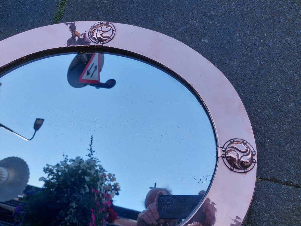An oval Arts and Crafts wall mirror featuring a polished copper frame embellished with four circular Celtic swirl motif roundels. View III