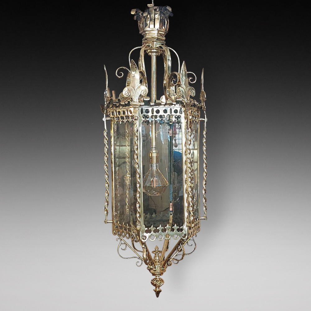 A hexagonal Victorian hanging brass lantern featuring glass panels, twisted corner columns, decorative scrollwork, and a central light bulb fitting.