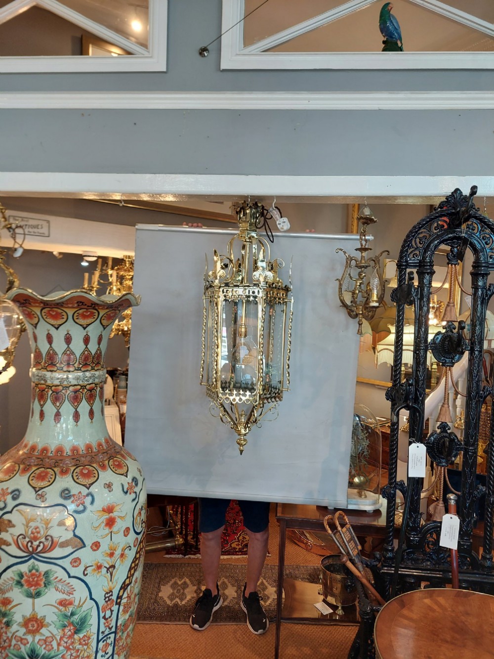 A hexagonal Victorian hanging brass lantern featuring glass panels, twisted corner columns, decorative scrollwork, and a central light bulb fitting. View V