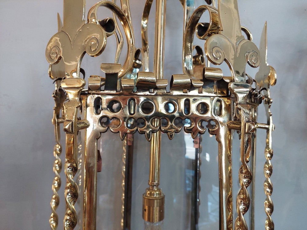 A hexagonal Victorian hanging brass lantern featuring glass panels, twisted corner columns, decorative scrollwork, and a central light bulb fitting. View VI
