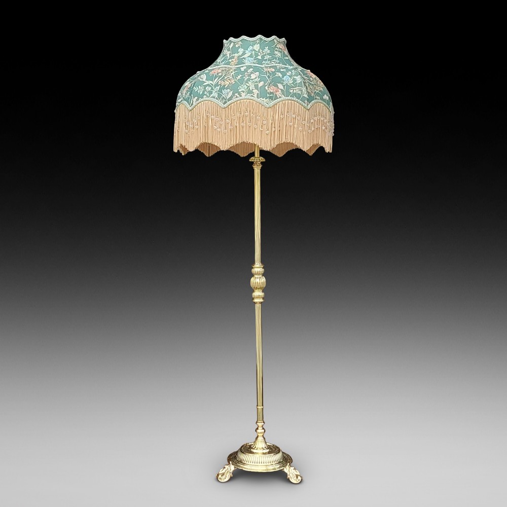 A Victorian brass standard floor lamp featuring a fluted column base and a scalloped green floral fabric shade with tassel fringe.