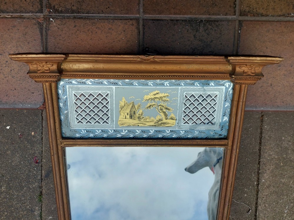 A Regency giltwood pier mirror featuring an architectural cornice, fluted side pilasters, and a blue verre eglomise glass frieze with a landscape scene. View II