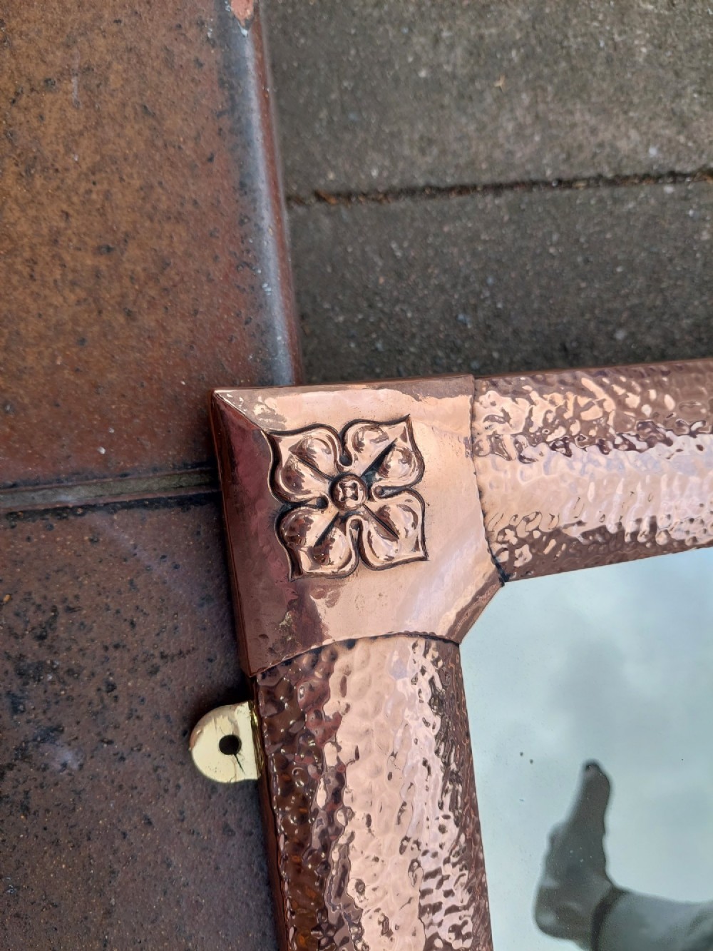 A rectangular wall mirror with a hand-beaten copper frame featuring raised floral rosettes at each corner. View III
