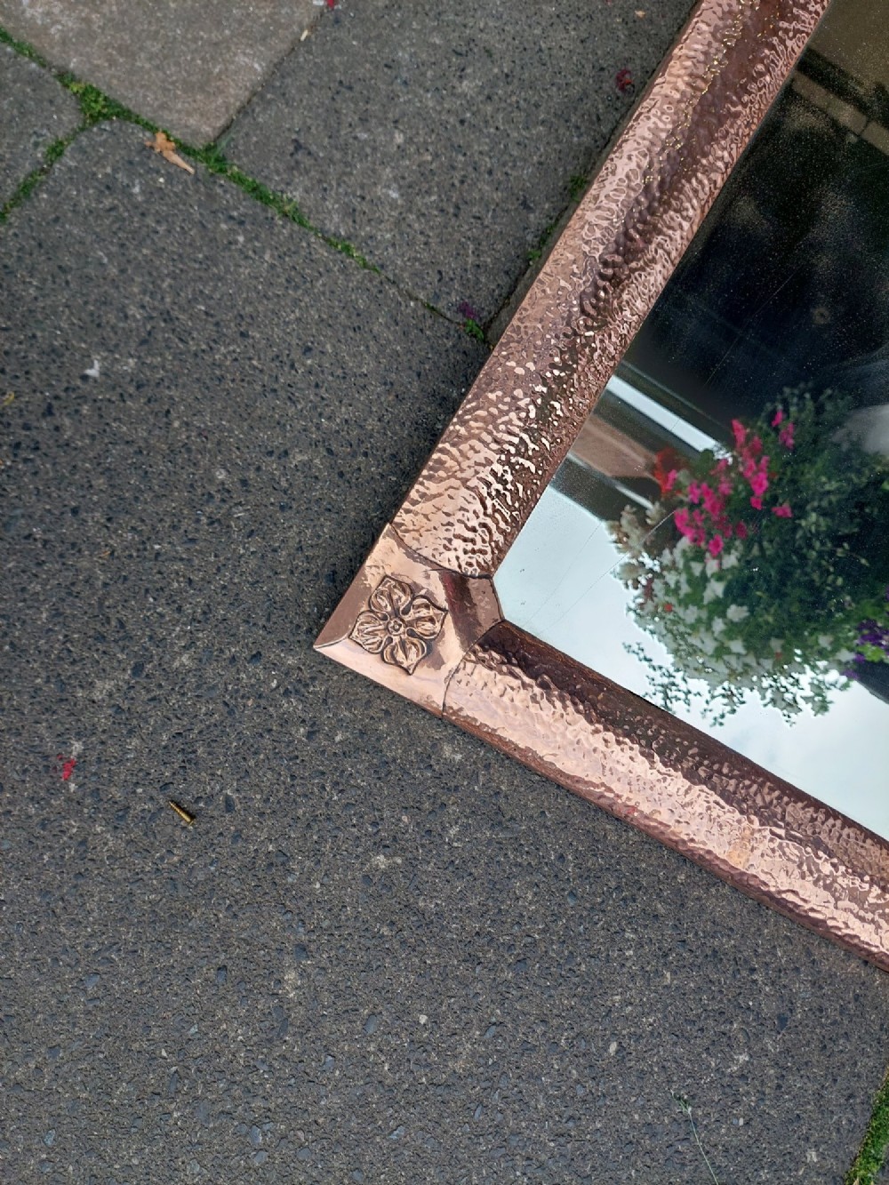 A rectangular wall mirror with a hand-beaten copper frame featuring raised floral rosettes at each corner. View V