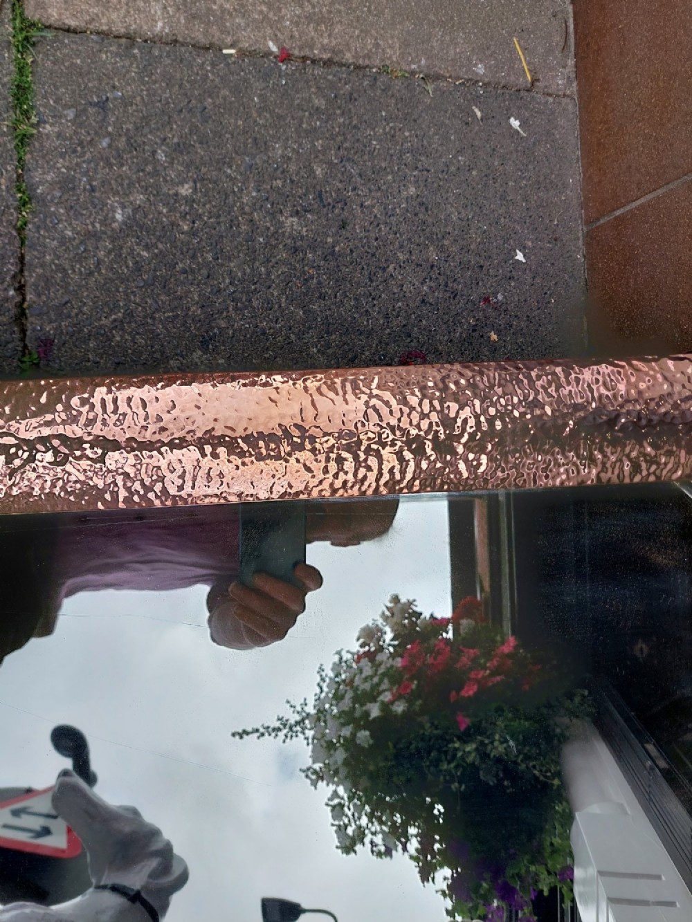 A rectangular wall mirror with a hand-beaten copper frame featuring raised floral rosettes at each corner. View VI