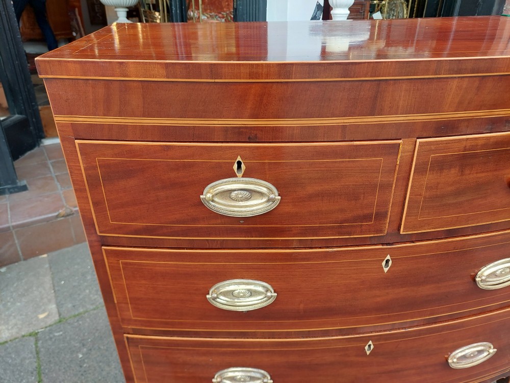 A Regency mahogany bow front chest featuring two short over two long drawers with oval brass handles, inlaid stringing, and splayed bracket feet. View III