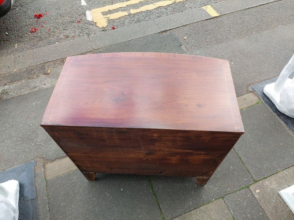 A Regency mahogany bow front chest featuring two short over two long drawers with oval brass handles, inlaid stringing, and splayed bracket feet. View V