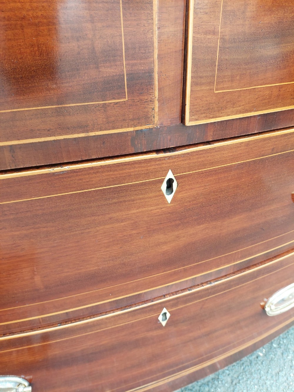 A Regency mahogany bow front chest featuring two short over two long drawers with oval brass handles, inlaid stringing, and splayed bracket feet. View VIII
