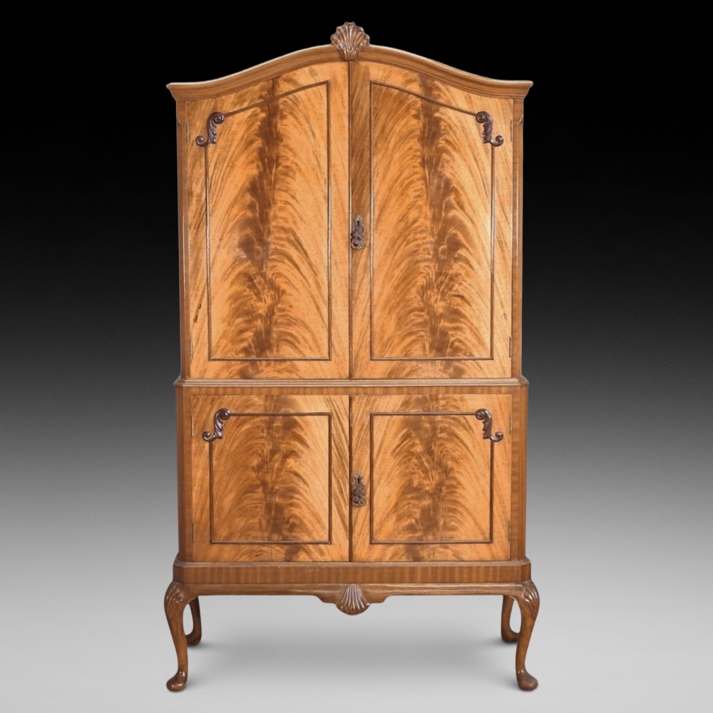 A mid-20th-century flame walnut drinks cabinet featuring double doors, carved shell motifs, and cabriole legs.