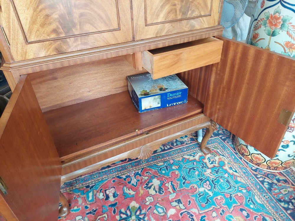 A mid-20th-century flame walnut drinks cabinet featuring double doors, carved shell motifs, and cabriole legs. View VII
