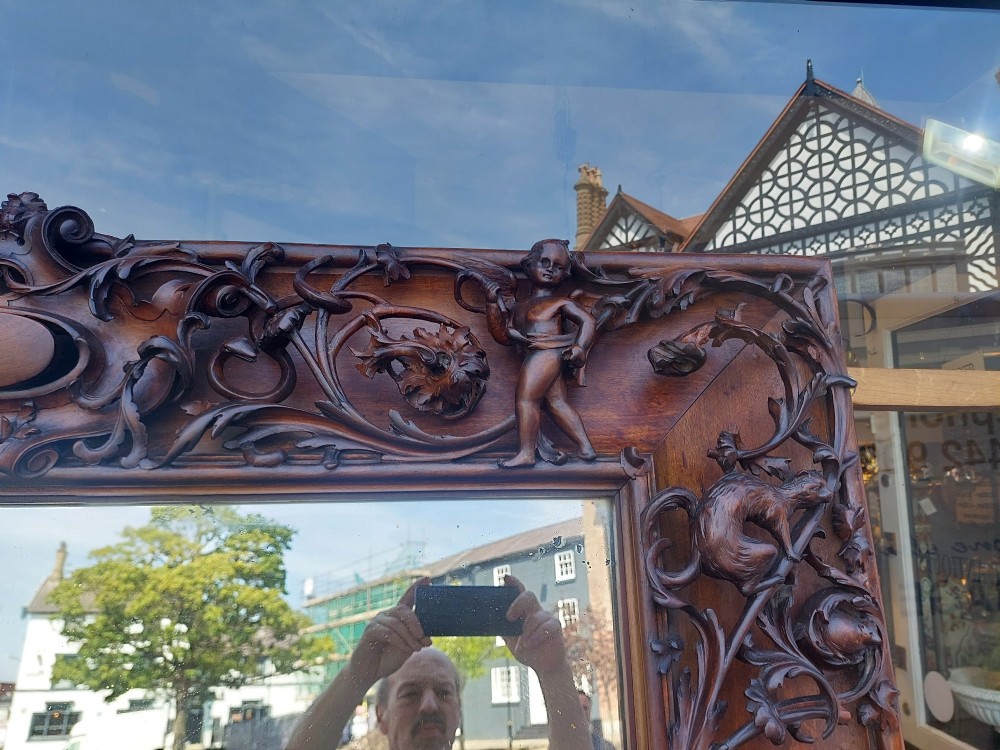A large rectangular Victorian wall mirror set within a deeply carved dark walnut frame adorned with cherub figures and foliate relief details. View XII