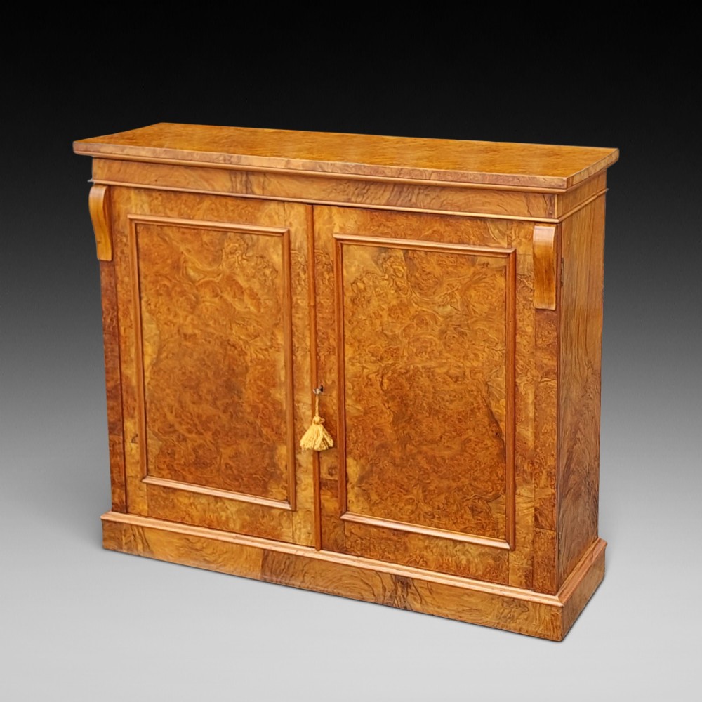 A Victorian burr walnut salon cabinet featuring two framed panel doors, carved support brackets, and a flat plinth base.