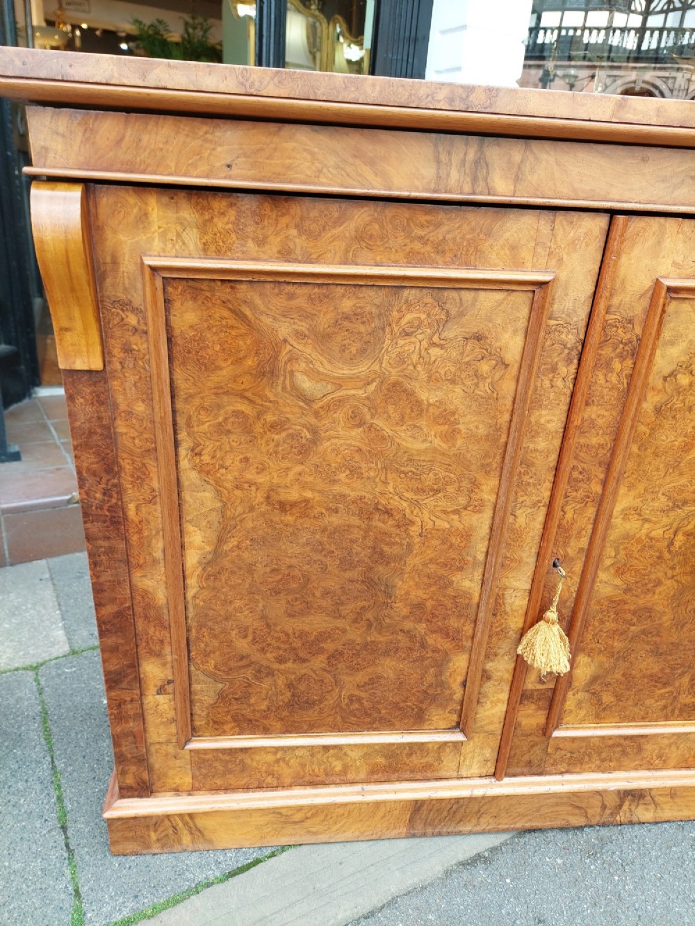 A Victorian burr walnut salon cabinet featuring two framed panel doors, carved support brackets, and a flat plinth base. View IV