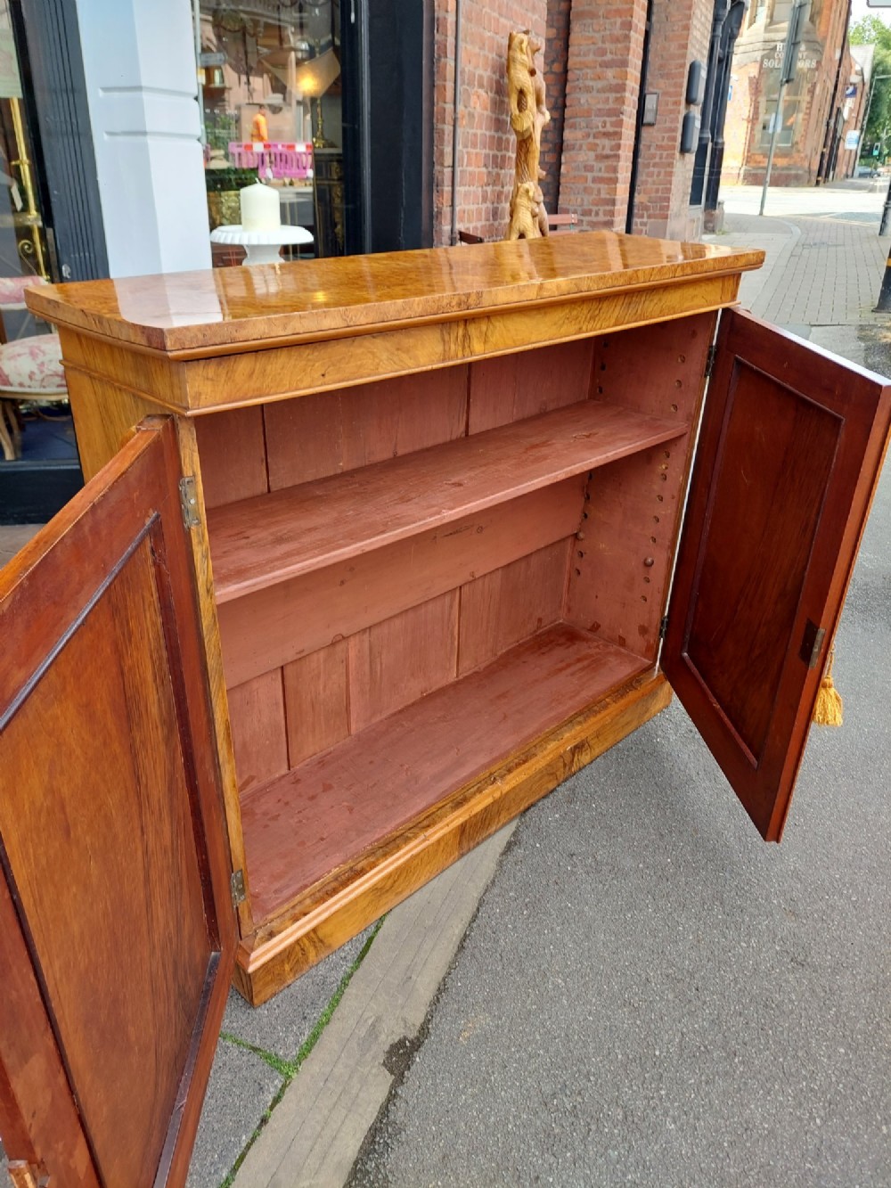 A Victorian burr walnut salon cabinet featuring two framed panel doors, carved support brackets, and a flat plinth base. View V