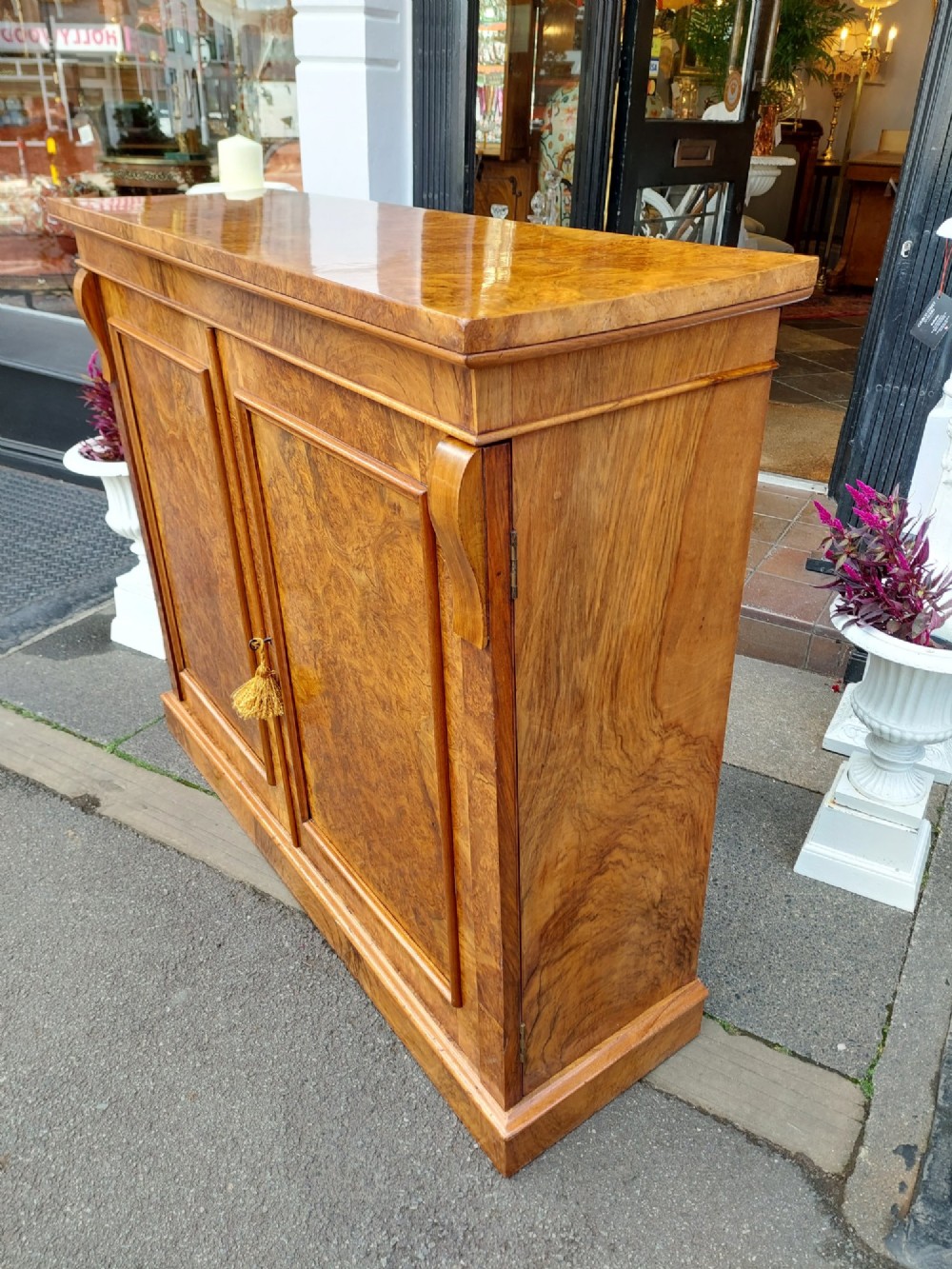 A Victorian burr walnut salon cabinet featuring two framed panel doors, carved support brackets, and a flat plinth base. View VII