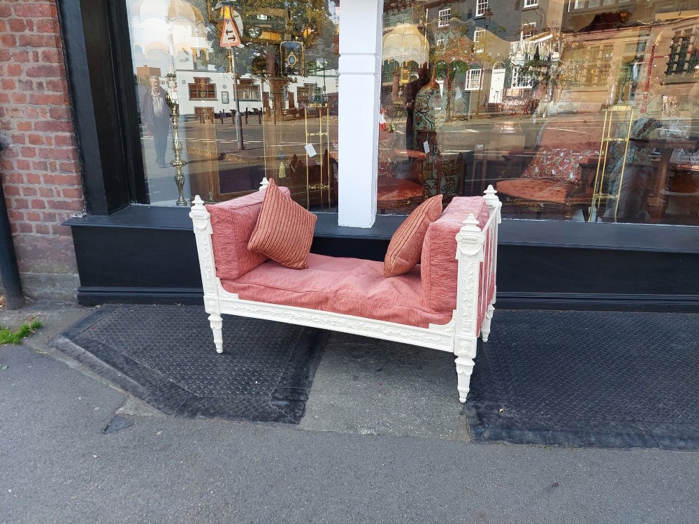 A white painted late Victorian cast iron daybed with relief mouldings, finials, fluted legs, and pink cushion upholstery. View II