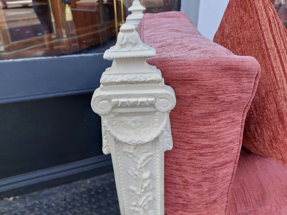 A white painted late Victorian cast iron daybed with relief mouldings, finials, fluted legs, and pink cushion upholstery. View V