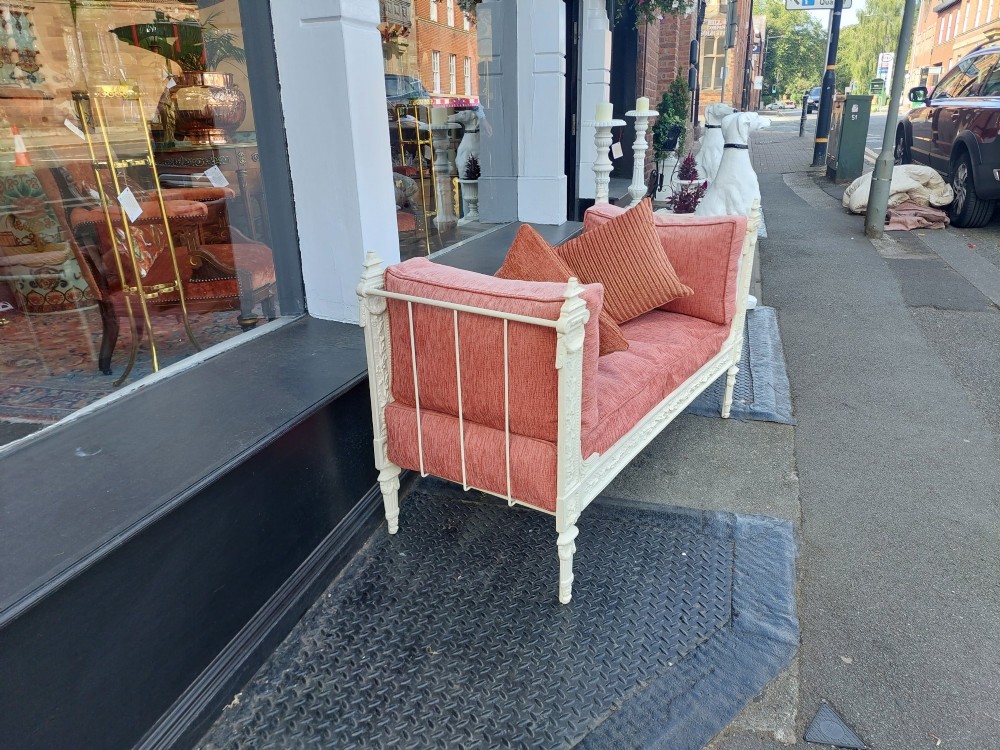 A white painted late Victorian cast iron daybed with relief mouldings, finials, fluted legs, and pink cushion upholstery. View VI