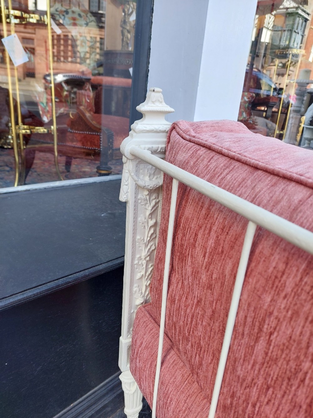 A white painted late Victorian cast iron daybed with relief mouldings, finials, fluted legs, and pink cushion upholstery. View VII