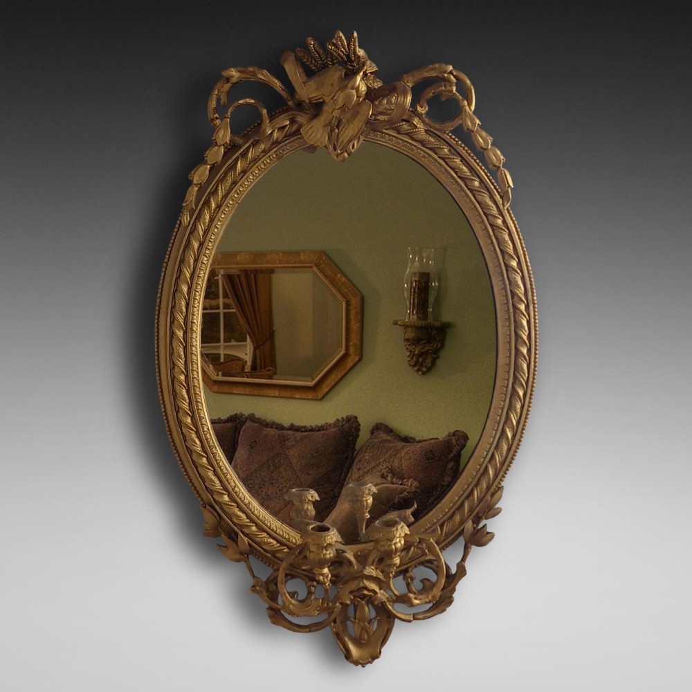 A pair of late nineteenth-century oval giltwood girandole mirrors featuring ribbon crests and twin candle arms at the base. View II