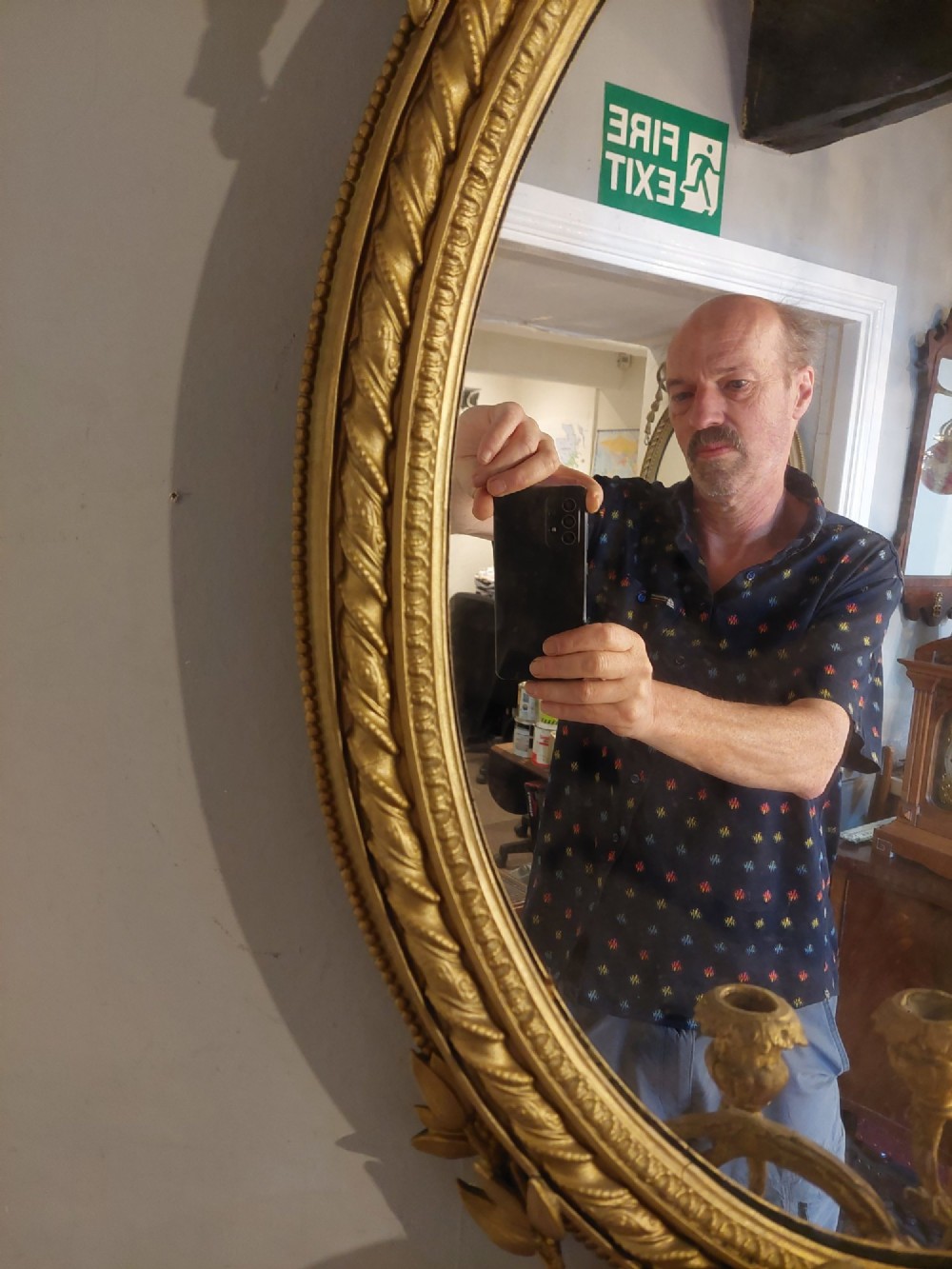 A pair of late nineteenth-century oval giltwood girandole mirrors featuring ribbon crests and twin candle arms at the base. View V