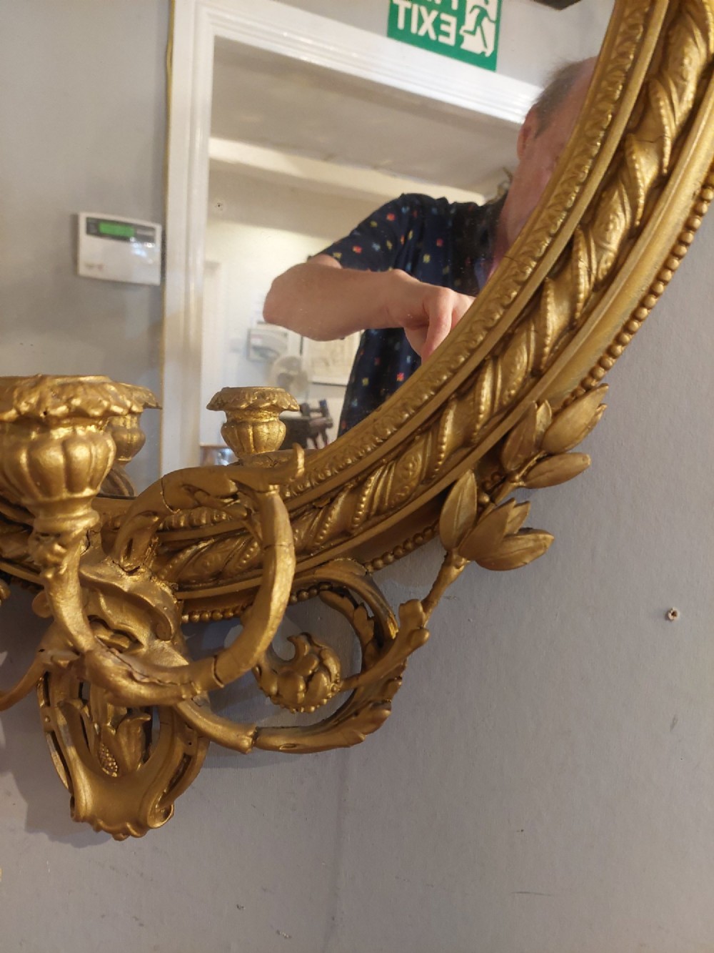 A pair of late nineteenth-century oval giltwood girandole mirrors featuring ribbon crests and twin candle arms at the base. View VIII