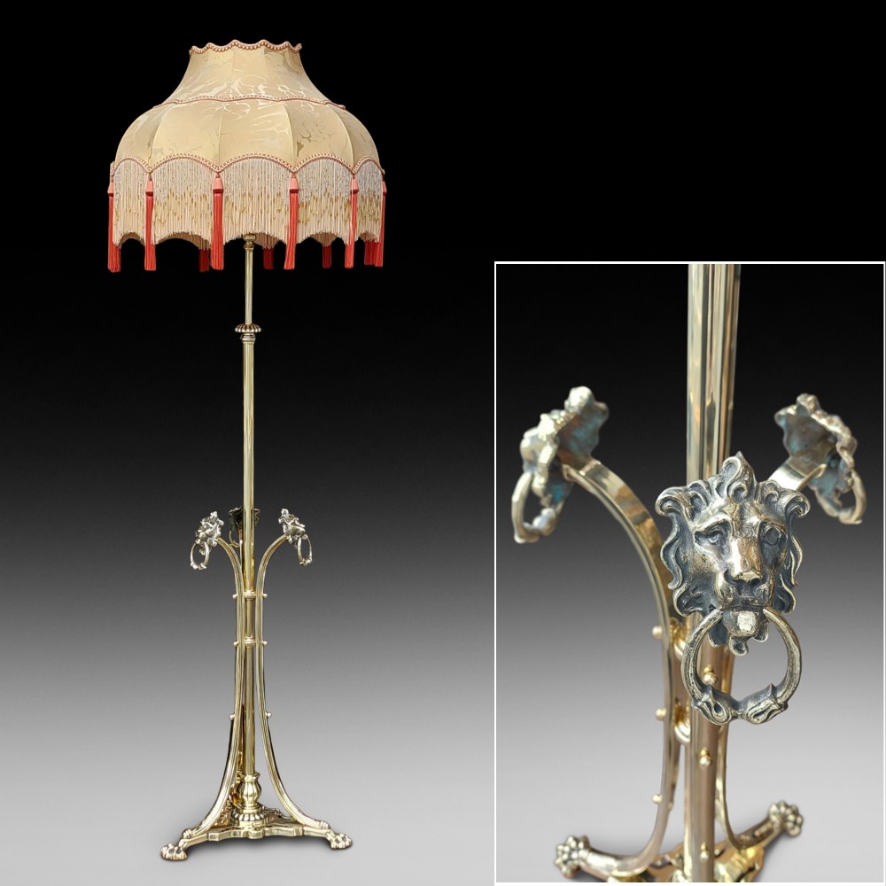 A Victorian brass standard floor lamp featuring a tripod claw-foot base, decorative mid-stem mounts, and a cream domed fabric shade trimmed with fringe and red tassels. View II