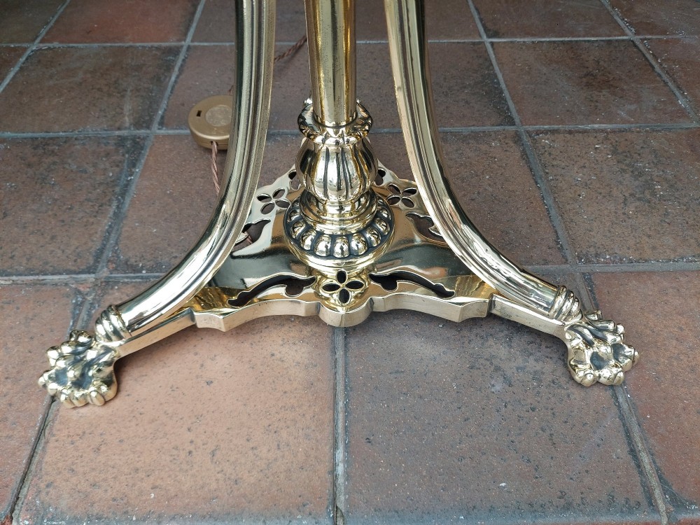 A Victorian brass standard floor lamp featuring a tripod claw-foot base, decorative mid-stem mounts, and a cream domed fabric shade trimmed with fringe and red tassels. View VI