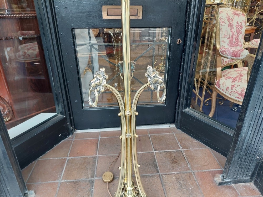 A Victorian brass standard floor lamp featuring a tripod claw-foot base, decorative mid-stem mounts, and a cream domed fabric shade trimmed with fringe and red tassels. View VII