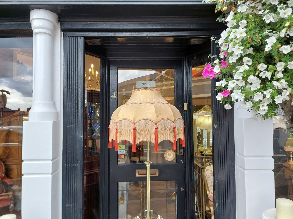 A Victorian brass standard floor lamp featuring a tripod claw-foot base, decorative mid-stem mounts, and a cream domed fabric shade trimmed with fringe and red tassels. View X