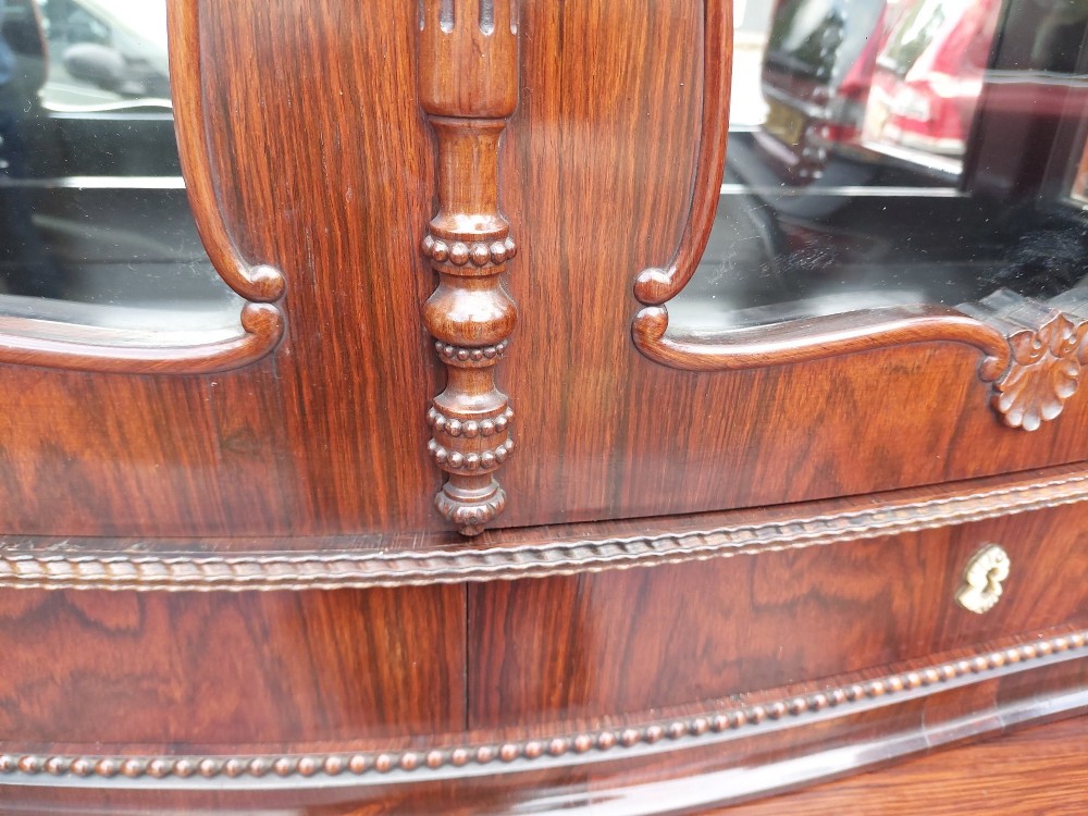 A two-tier Biedermeier rosewood display cabinet featuring a glazed upper section with a carved cresting above a two-door cupboard base. View VI